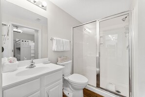 Bathroom features a large mirror, sink, toilet, and glass-enclosed shower stall.