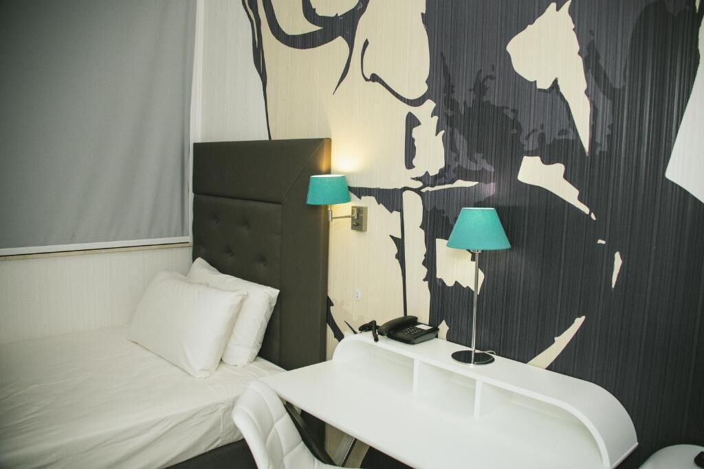 Habitación de hotel con una cama, un escritorio con lámpara y una pared con un diseño abstracto grande.