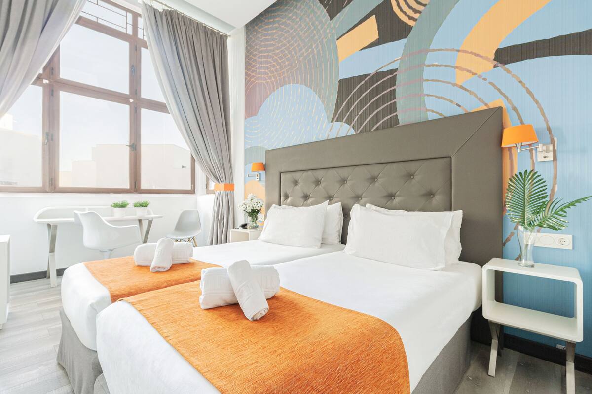 A hotel room with a large bed, two bedside tables, a desk, and a window with curtains.