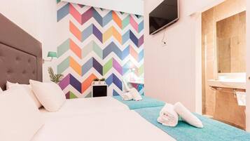 A hotel room with a bed, a TV mounted on the wall, a shower area, and a colorful chevron-patterned wall.
