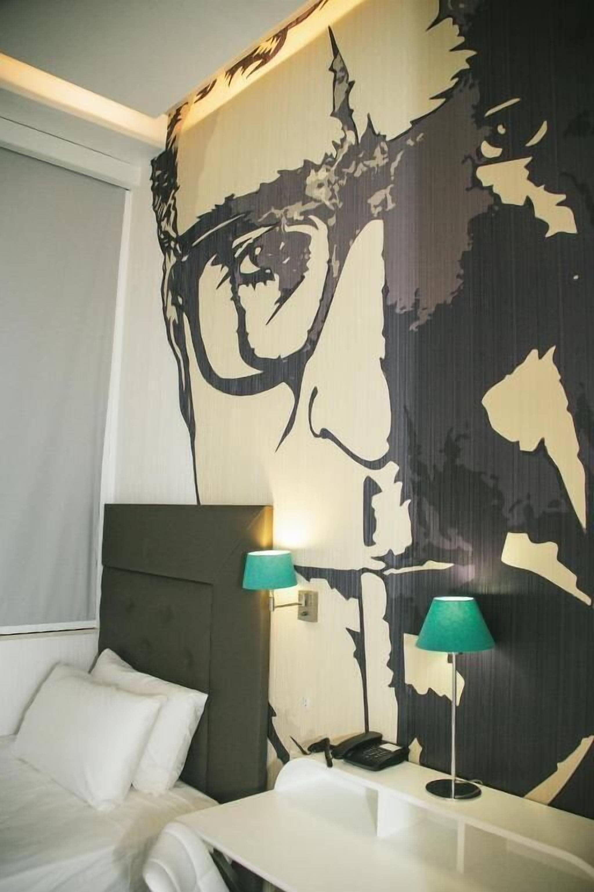 A hotel room with a large abstract wall mural, a bed with white linens, two bedside lamps, and a bedside telephone.