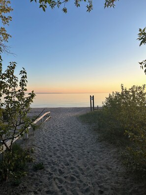 A sandy beach path leading to the sea with a wooden structure on the right.