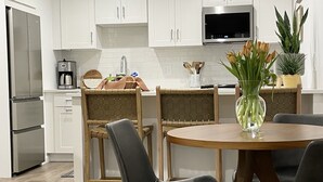 Eine moderne Küche mit weißen Schränken, einem Edelstahlkühlschrank, einer Mikrowelle und einem Essbereich mit einem runden Holztisch und schwarzen Stühlen.