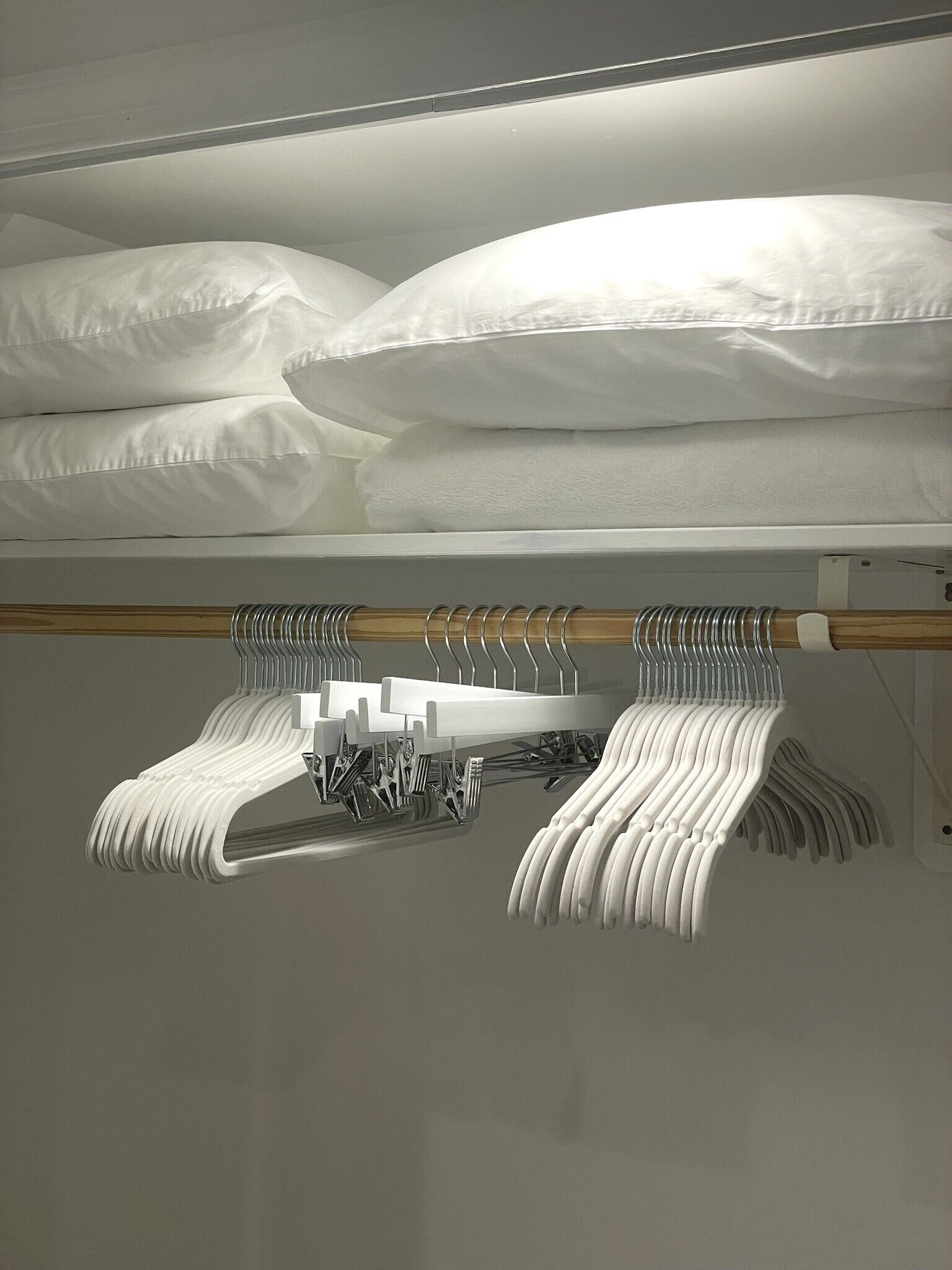 A neatly organized closet with hanging clothes and a bed with white linens.