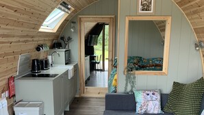 A compact, wooden interior with a kitchenette, a sofa, and a large mirror. - Tawny Owl Pod with Hot Tub (Glencruitten)