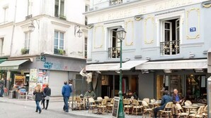 Un café con terraza, un letrero que dice 'Au Rocher De Cancal' y una calle con gente caminando.