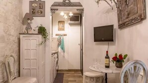 Un pasillo estrecho con una puerta blanca, una pequeña mesa con un televisor y una silla.
