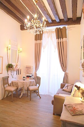 A cozy room with a wooden ceiling, a chandelier, a dining table with chairs, a sofa, and a bed.