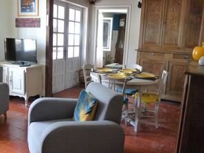 Un salon avec un canapé gris, un téléviseur posé sur un meuble, une table à manger avec des assiettes jaunes et un coin cuisine avec des meubles en bois.