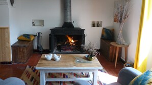 Ein gemütliches Wohnzimmer mit Kaminofen, Holzregalen, einem Tisch mit Dekoration und einem bunten Teppich.