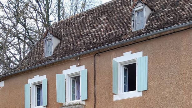 Ein Gebäude mit einer Steinaußenfassade, mehreren Fenstern mit Fensterläden und Außenplätzen mit Stühlen und Sonnenschirm.
