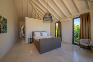 Een moderne slaapkamer met een groot bed, een hanglamp, een stoel en uitzicht op groen buiten.