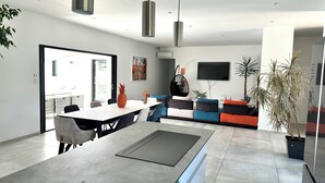 Una sala de estar moderna con comedor, un televisor grande y una planta en maceta.