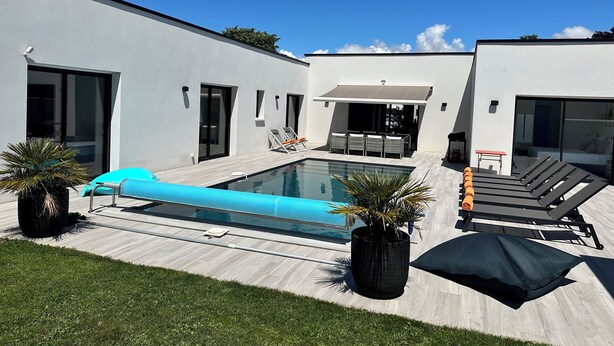 Area piscina moderna all'aperto, con una vasca rettangolare, poltrona relax e zona salotto coperta.