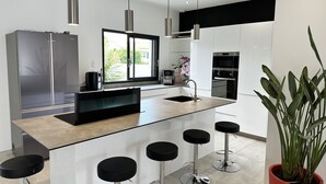 Una cocina moderna con una isla central, taburetes de bar, electrodomésticos de acero inoxidable e iluminación colgante.