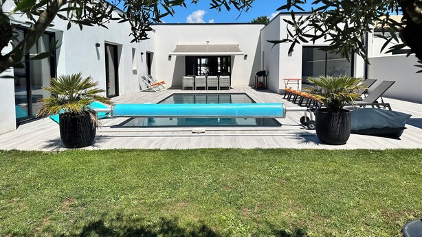 Un área de piscina moderna al aire libre con sillones de descanso, una mesa de comedor y plantas en macetas.