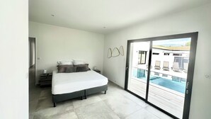 Un dormitorio moderno con una cama grande, una mesita de noche y vista a una piscina a través de un ventanal corredero.
