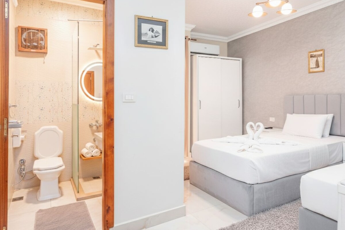 A modern bedroom with a bed, bedside tables, a wardrobe, and a bathroom with a toilet, sink, and shower.