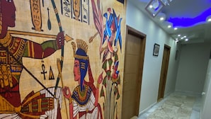 A hallway with a mural of ancient Egyptian figures, a patterned carpet, and modern lighting fixtures. - The GEM View Boutique (Giza)