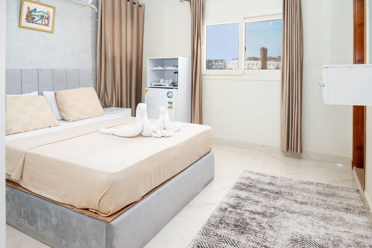 A bedroom with a bed, a small white cabinet, a window with a view, and a radiator.