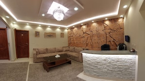 A living room with a sectional sofa, a coffee table, a stone accent wall with hieroglyphs, a chandelier, and recessed lighting. - The GEM View Boutique (Giza)