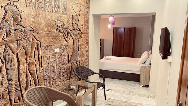 A room with a bed, a chair, a table, and a wall with ancient Egyptian carvings. - The GEM View Boutique (Giza)
