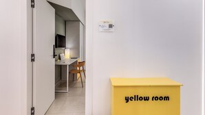 A room with a yellow room sign, a door leading to a kitchen, and a QR code on the wall. - National Square Napoli (Naples)