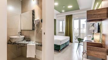 Ein modernes Hotelzimmer mit einem Badezimmer, das ein Waschbecken, einen Spiegel und einen Fön bietet. Das Zimmer verfügt über ein Bett, grüne Vorhänge und einen Blick auf die Stadt.