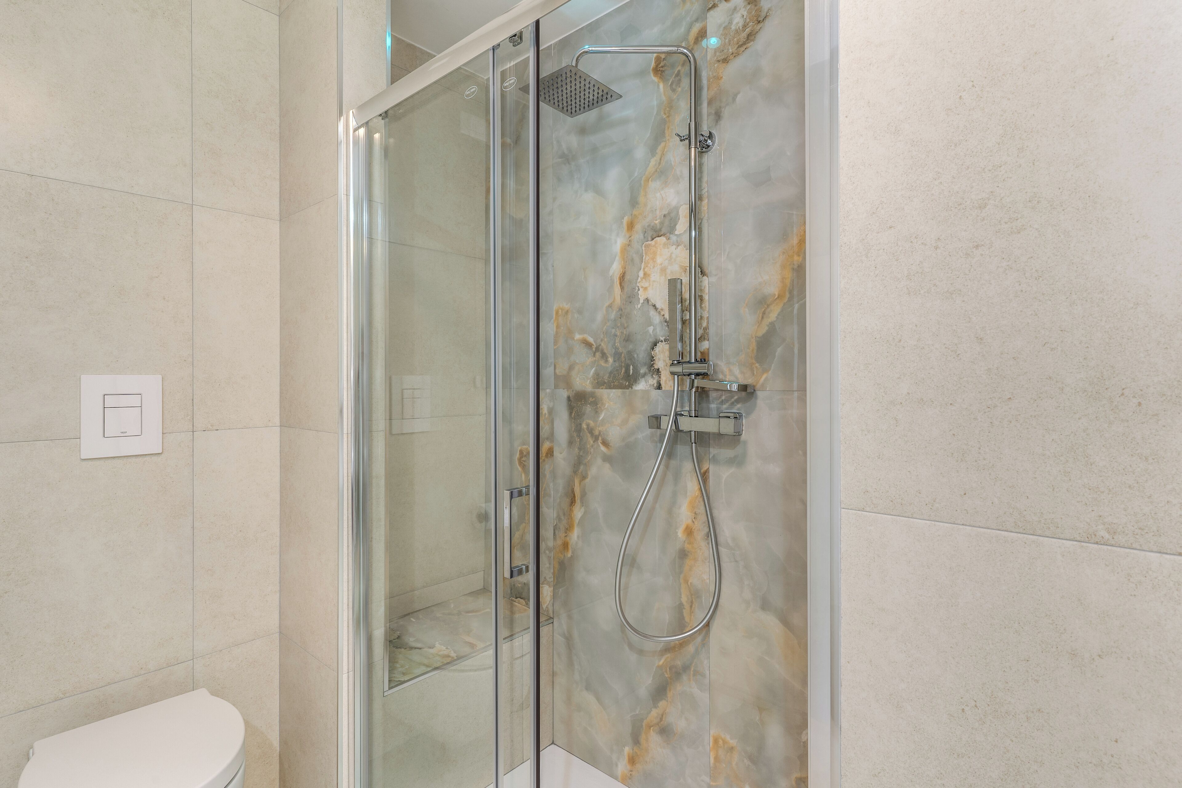 Une salle de bain moderne avec une douche à parois de verre, des murs en marbre et des toilettes blanches.