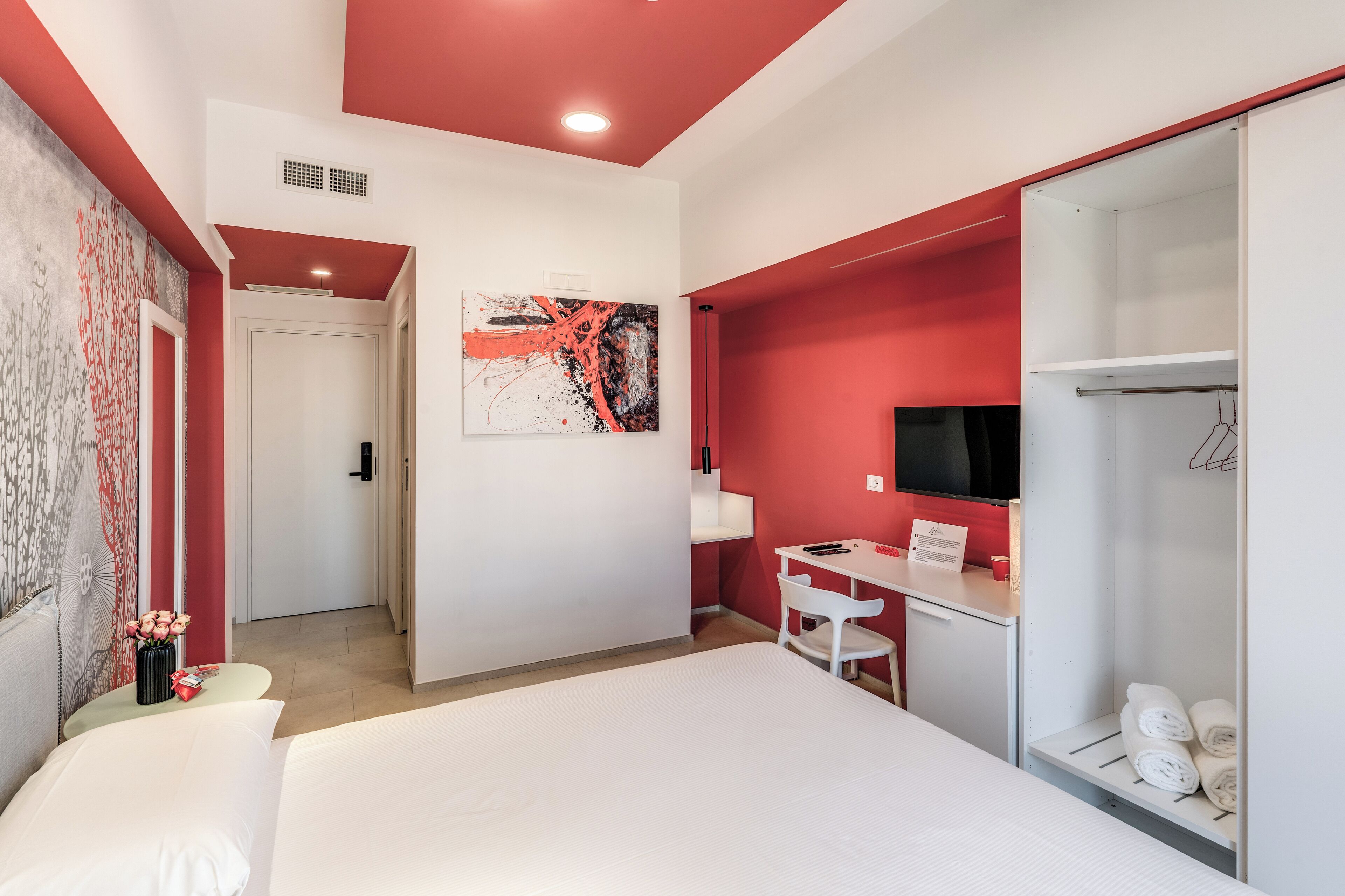 Ein modernes Hotelzimmer mit einem großen Bett, einem Schreibtisch mit Stuhl, einem Fernseher und einem Kleiderschrank.