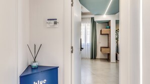 A hotel hallway with a blue room sign, a QR code, and a wooden shelf with decorative items. - National Square Napoli (Naples)