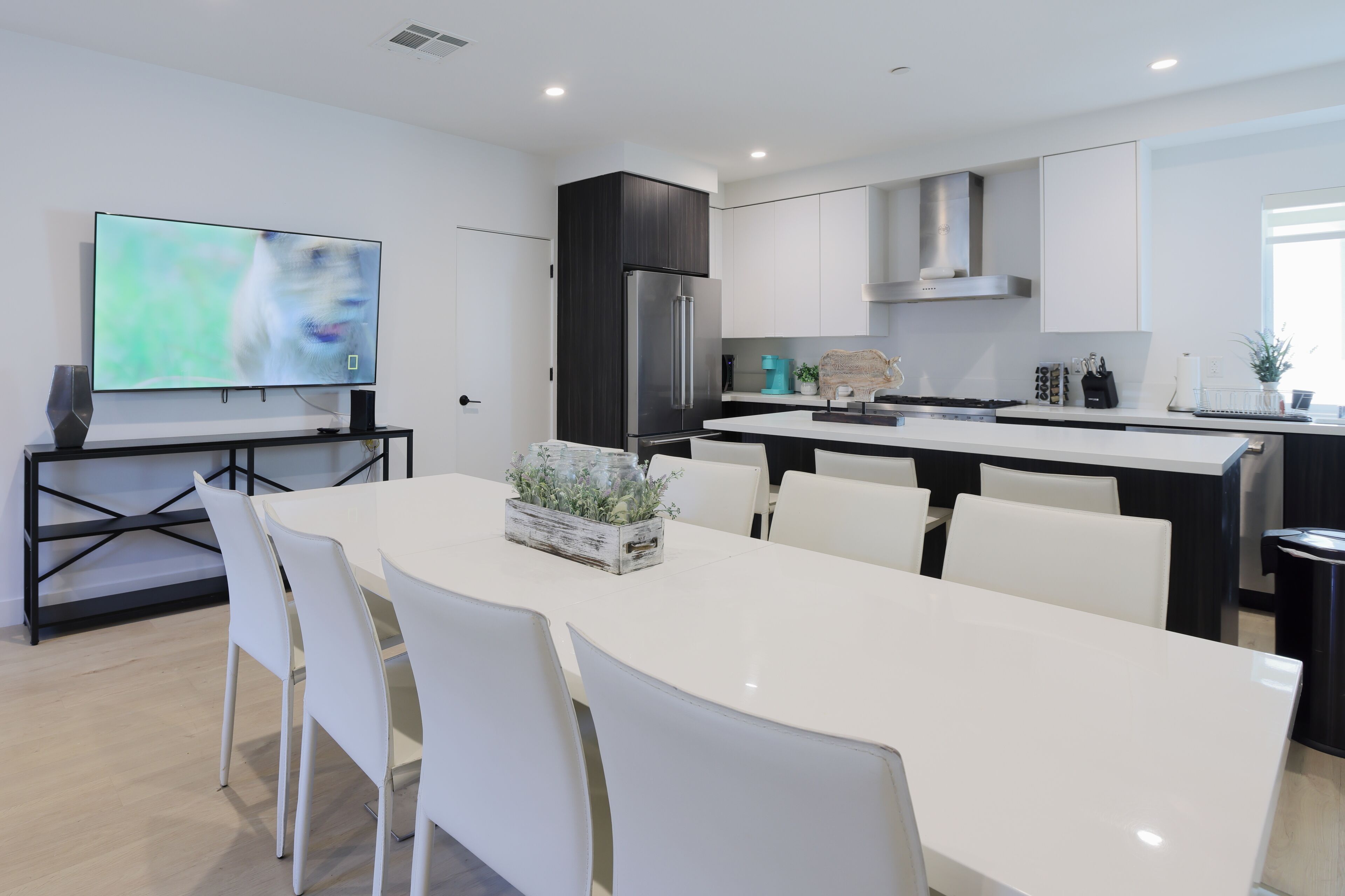 Een moderne keuken met witte kastjes, een roestvrijstalen koelkast, en een eethoek met witte stoelen en een tafel.