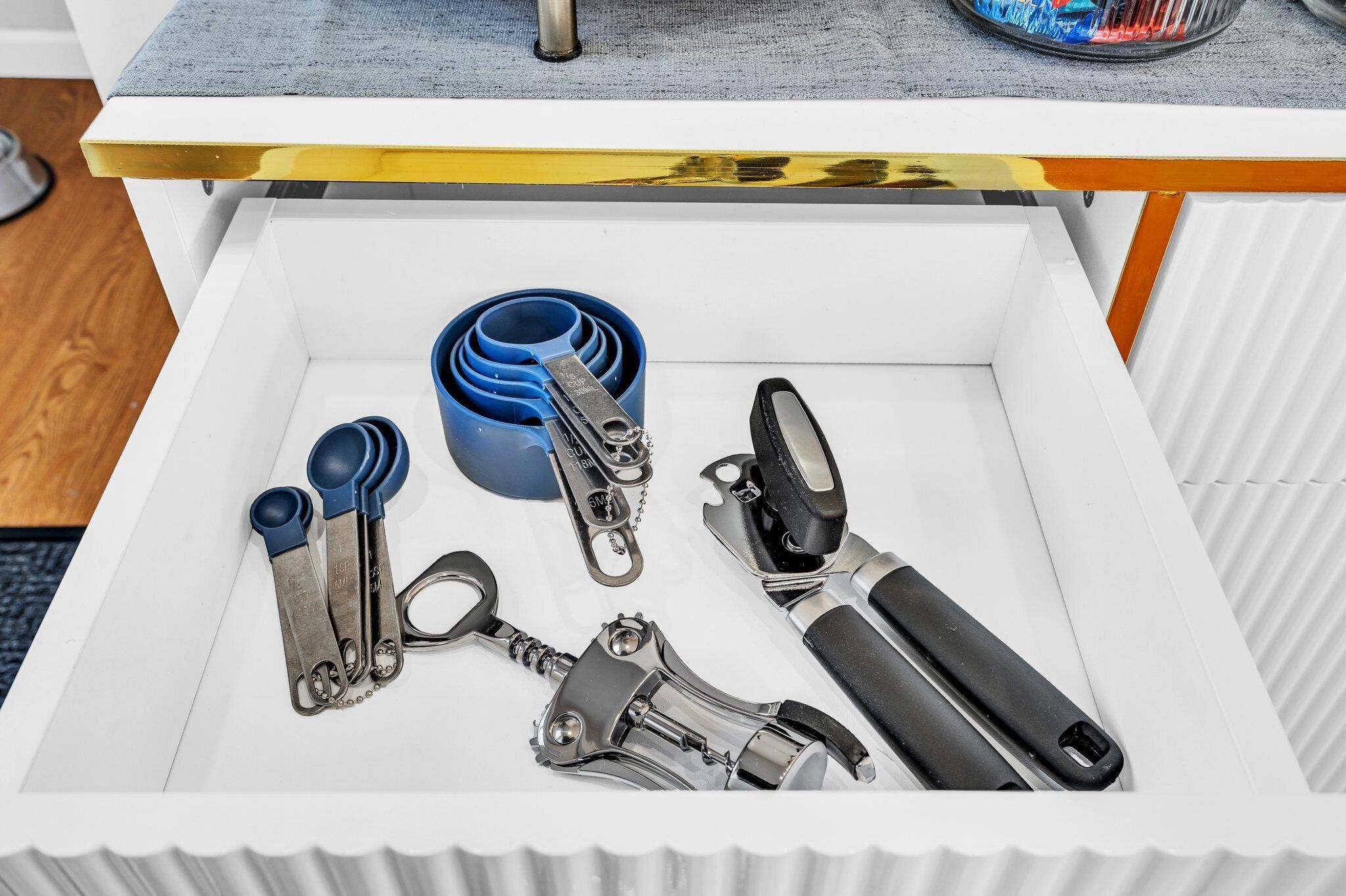 Un cajón con varias herramientas, incluyendo un dispensador de cinta azul, un abrelatas metálico y un abrelatas con mango negro.