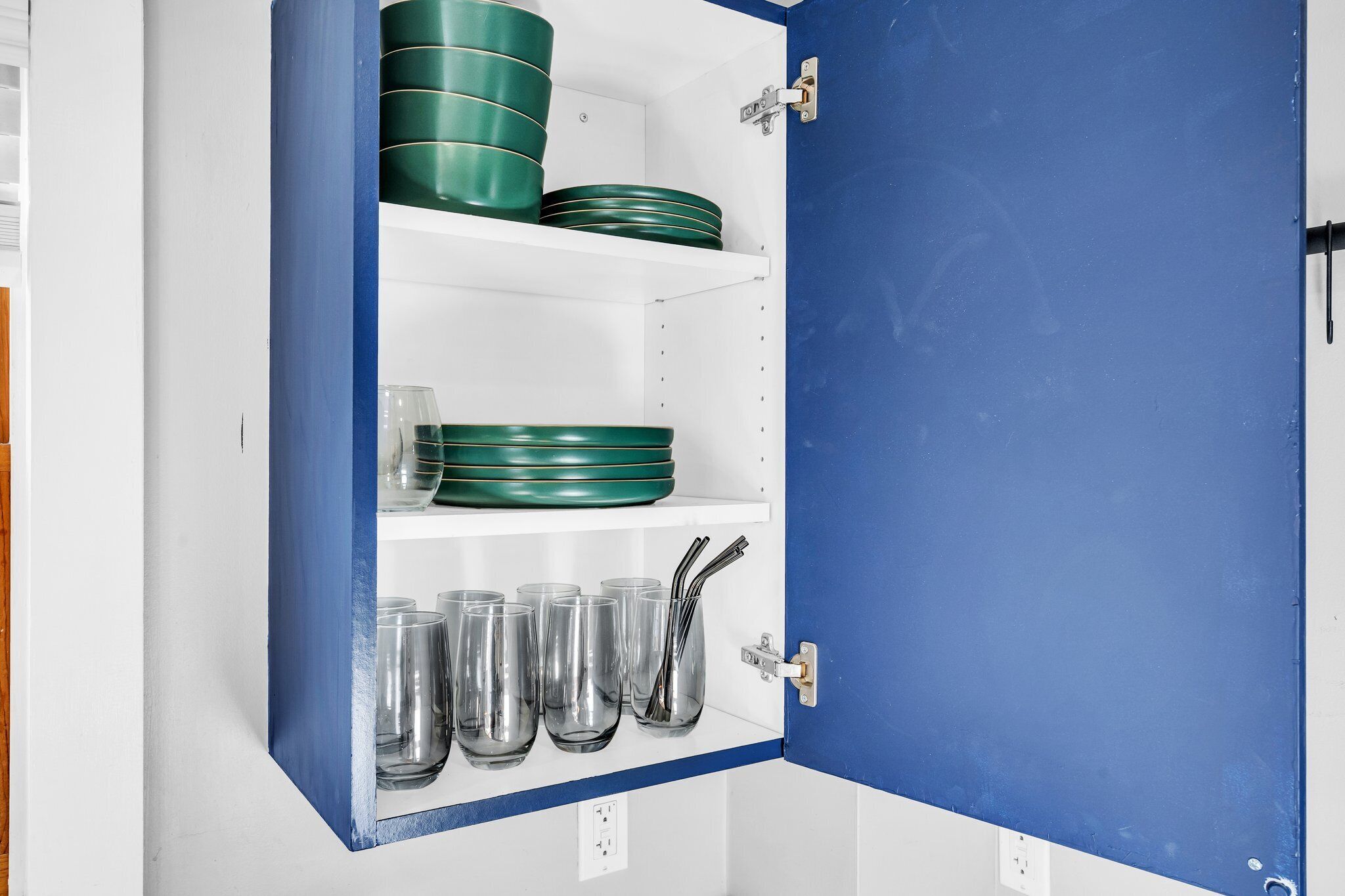 A cabinet with green plates and clear glasses.