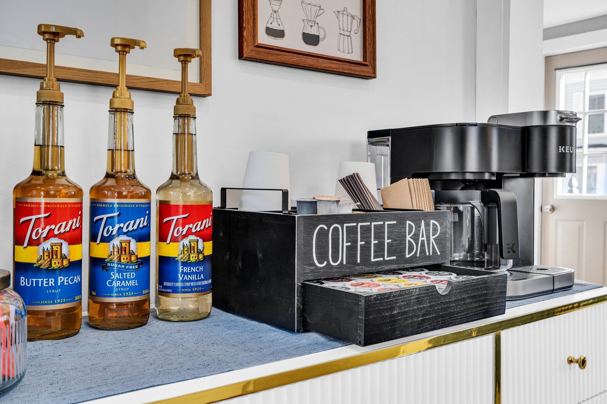 A kitchen counter with Torani syrup bottles, a coffee machine, and a coffee bar sign.