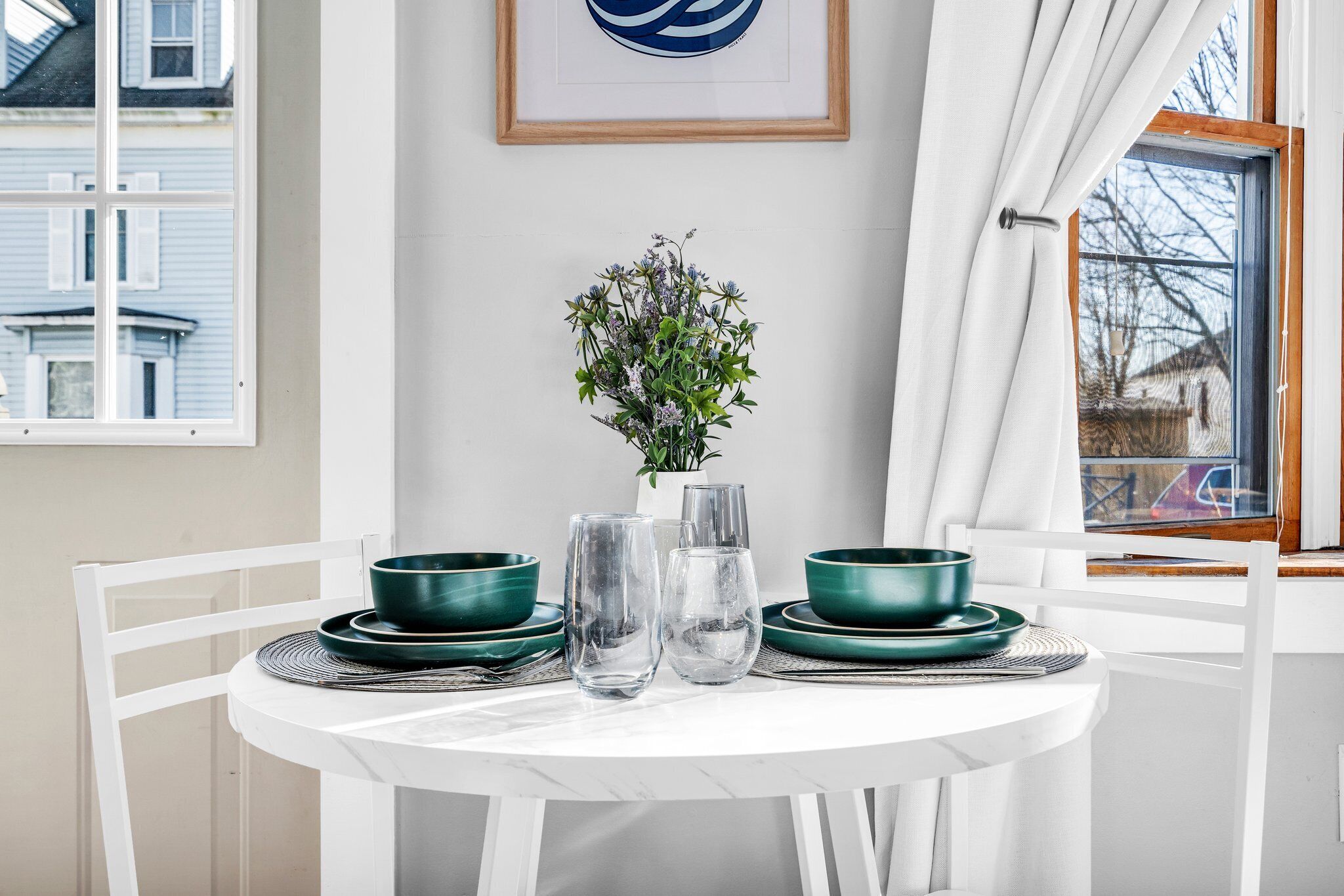 Une table à manger avec des bols verts, des verres transparents et un vase rempli de fleurs.