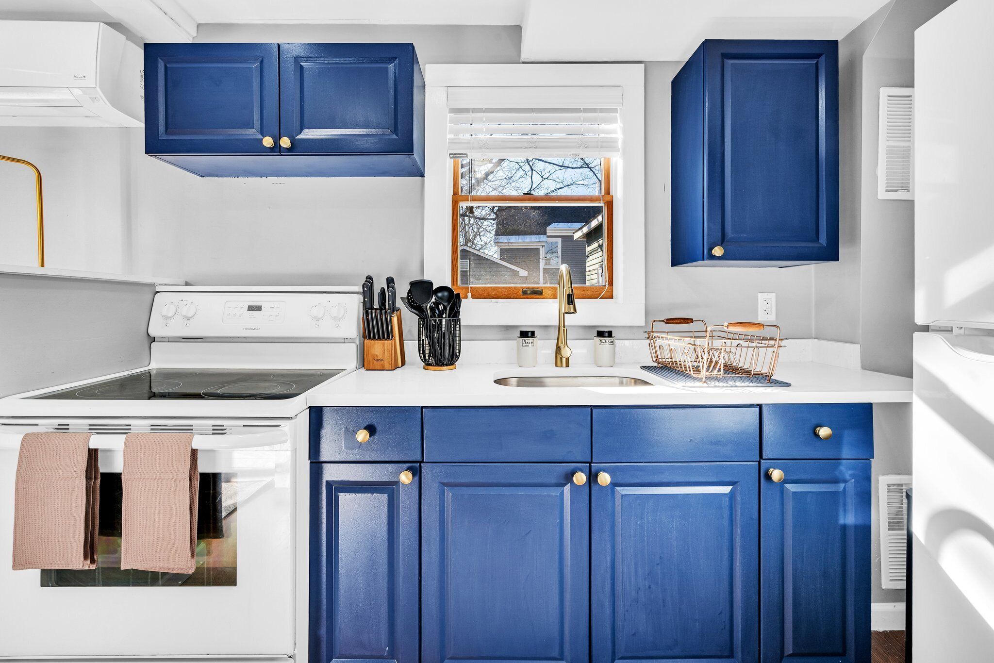 Una cocina con armarios blancos y azules, una estufa y un ventanal con persianas.