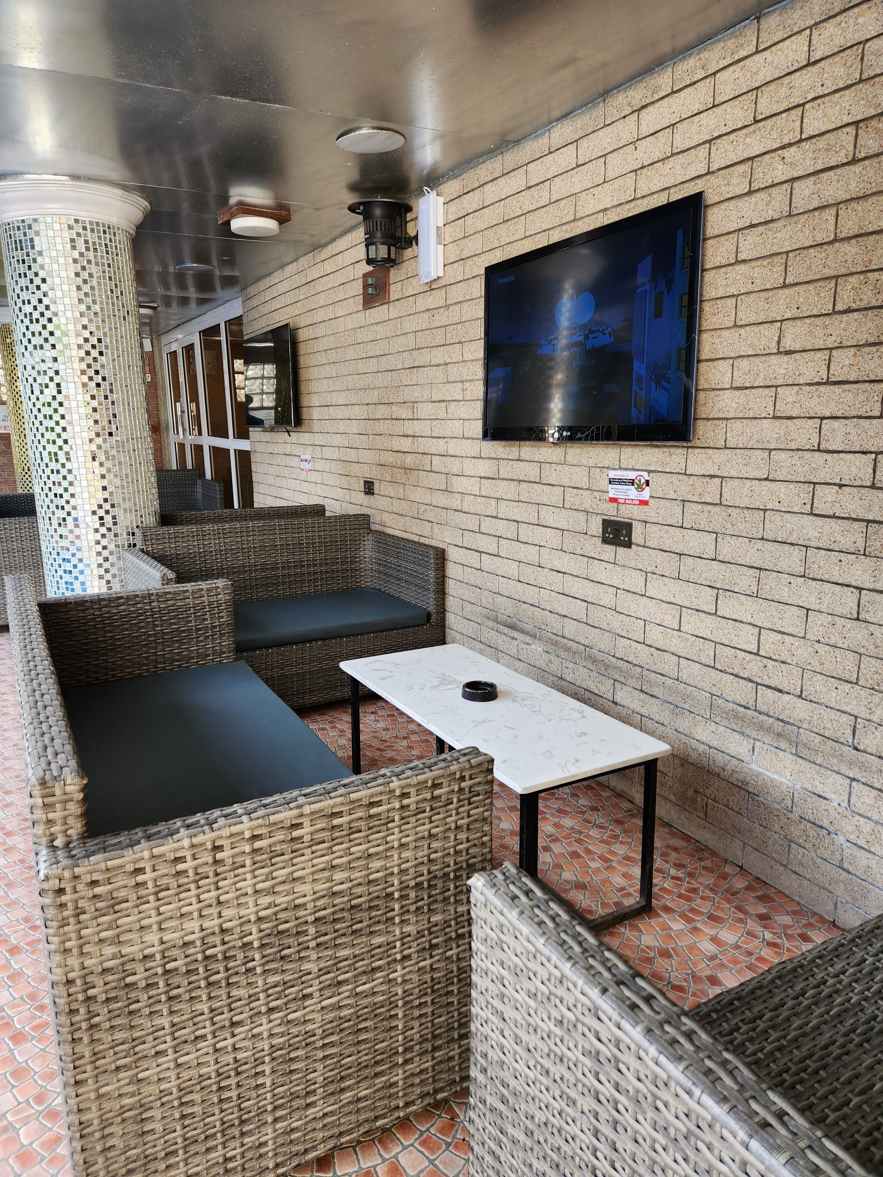 A modern outdoor seating area with wicker furniture and a flat-screen TV mounted on the wall.