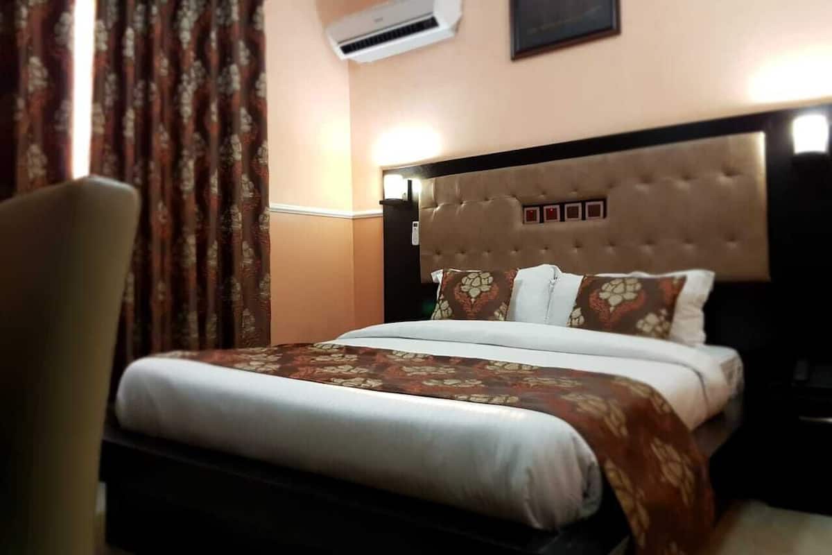A hotel room with a large bed, a headboard with a tufted design, and a wall-mounted air conditioner.