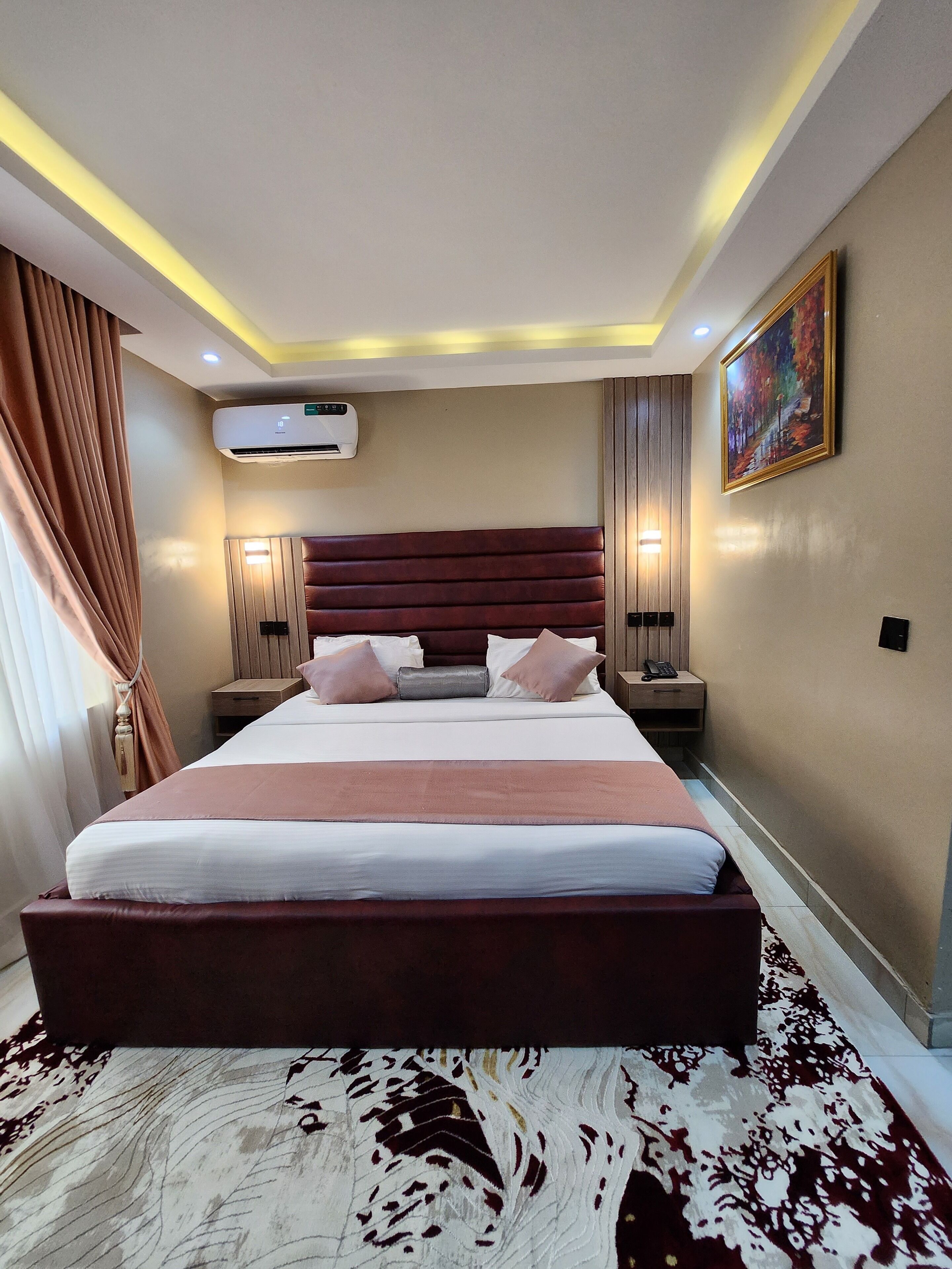 Een moderne hotelkamer met een groot bed, een wandairconditioner, een nachtkastje met lamp en een schilderij aan de muur.