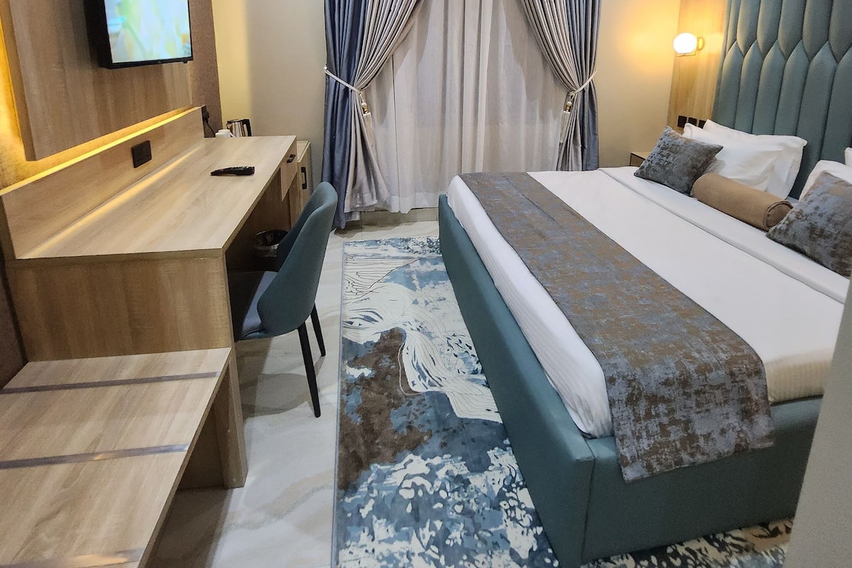 A hotel room with a bed, desk, chair, and a TV mounted on the wall.