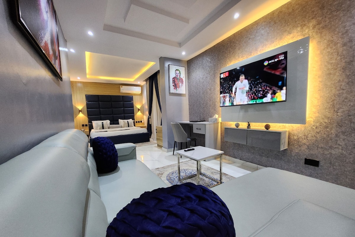 A modern living room with a large flat-screen TV mounted on the wall, a sofa, a coffee table, and a small desk area.