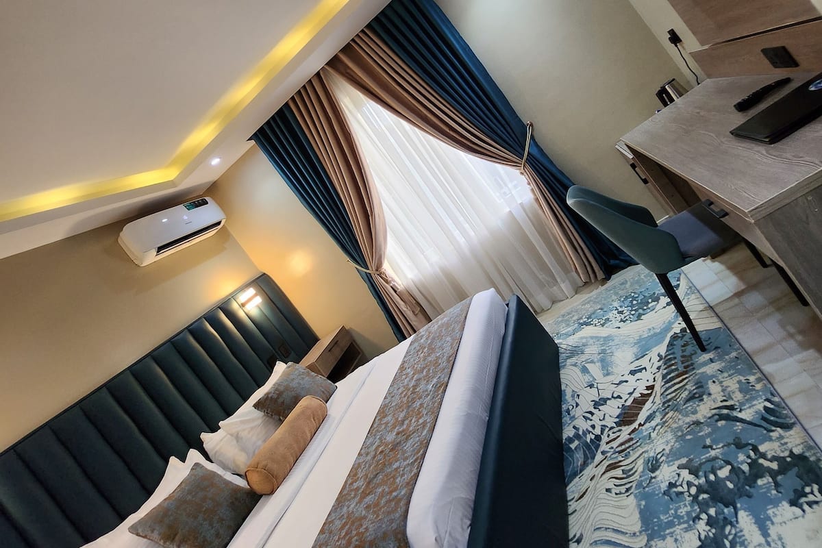 A modern hotel room with a bed, a desk, a flat-screen TV, and an air conditioning unit.