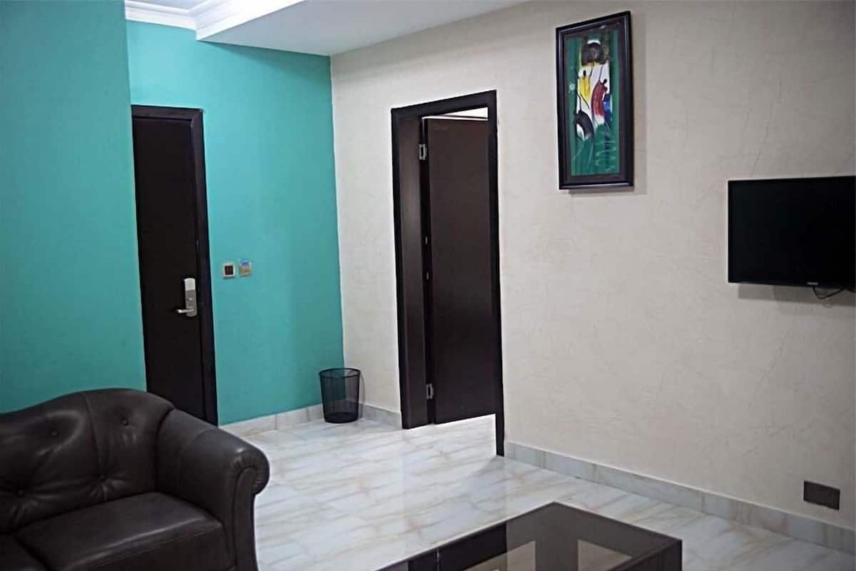 A room with teal walls, a black leather sofa, a marble floor, and a flat-screen TV mounted on the wall.
