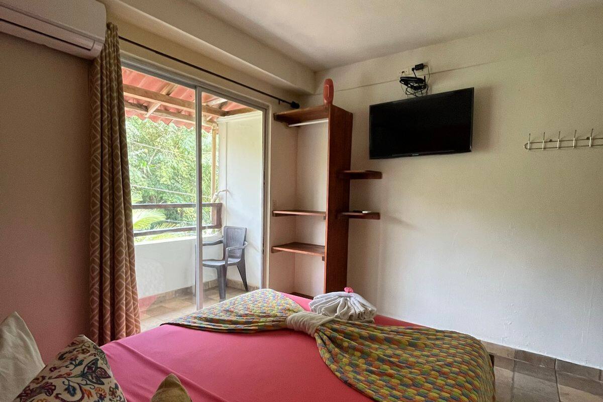 A bedroom with a bed, a TV, a balcony, and a chair.