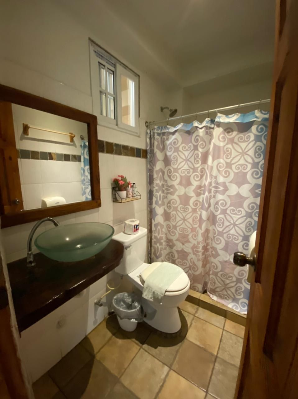 Un baño con lavamanos de vidrio, inodoro y cortina de ducha.