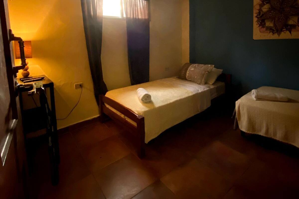 A small, dimly lit room with a single bed, a small table with a lamp, and a wall decoration.