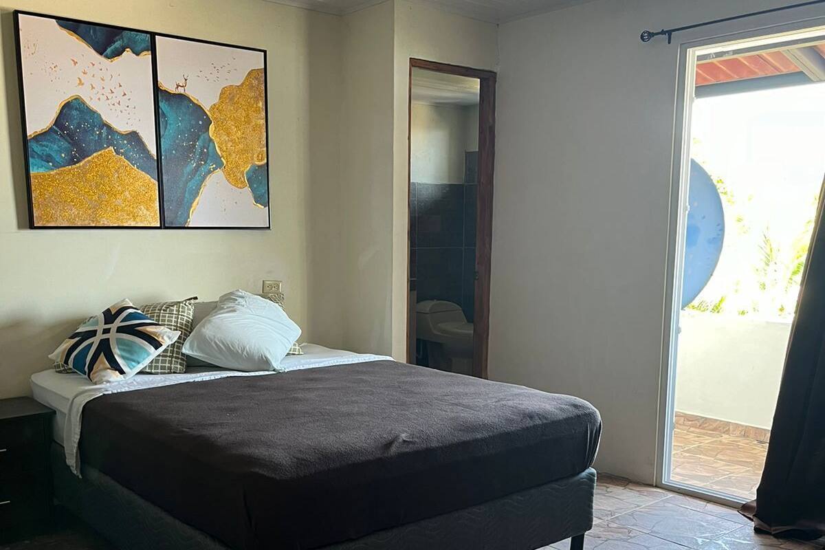 A bedroom with a bed, a nightstand, a mirror, and a window with a view.