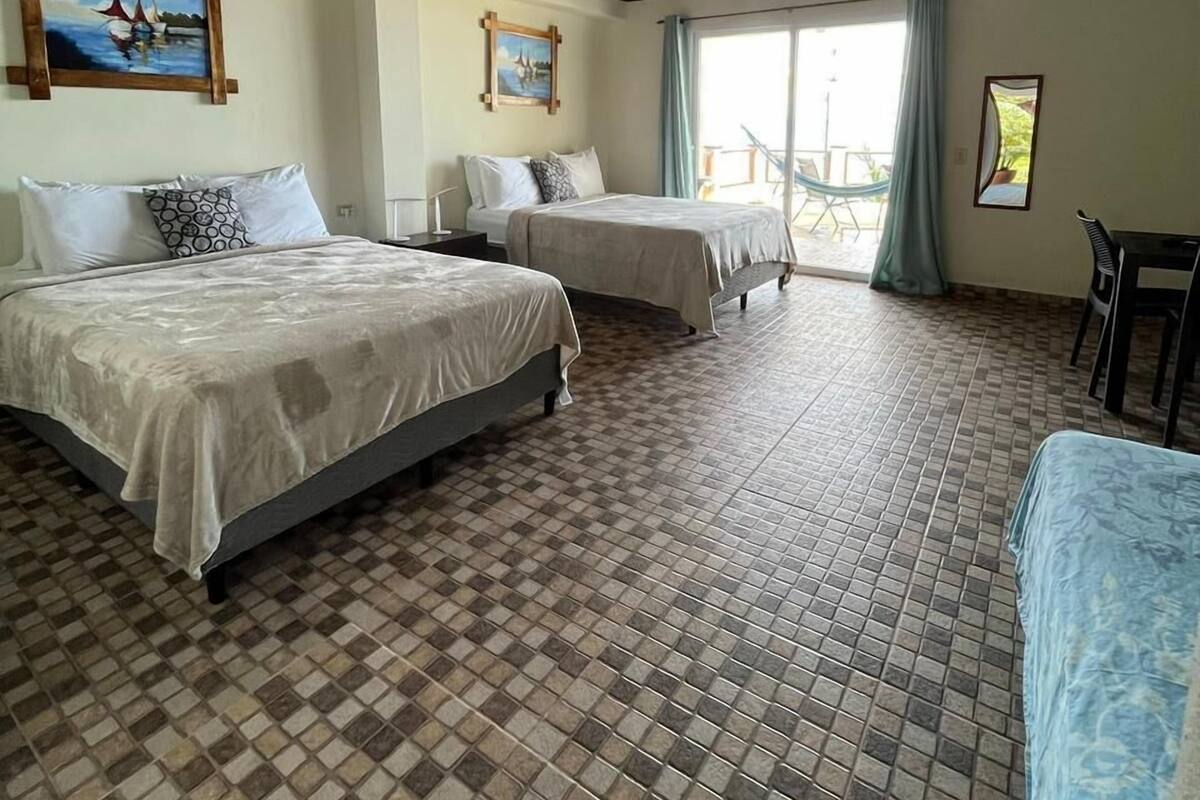 A hotel room with two beds, a balcony, and a dining area.