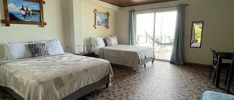 A hotel room with two beds, a dining area, and a view of the outdoors.